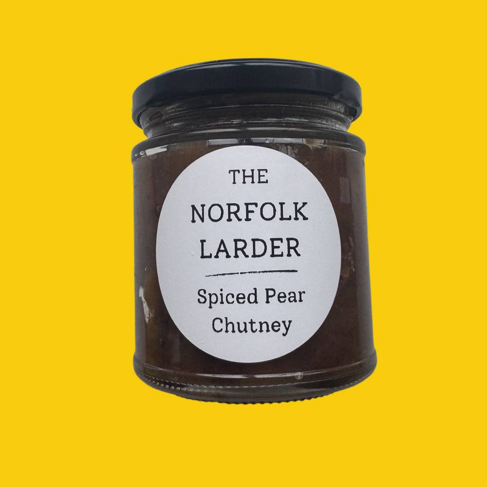 A glass jar of 'The Norfolk Larder' Spiced Pear Chutney with a black lid and a white circular label, set against a solid bright yellow background.